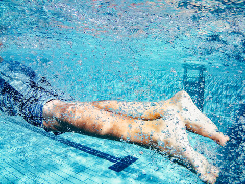 Close-up of a boy's legs swimming underwater in a swimming pool