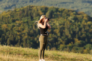 Blond kobieta fotografująca na tle lasów.