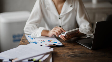 Fototapeta premium Close up of businesswoman or accountant hand holding pen working on calculator to calculate business data, accountancy document and laptop computer at office, business concept.