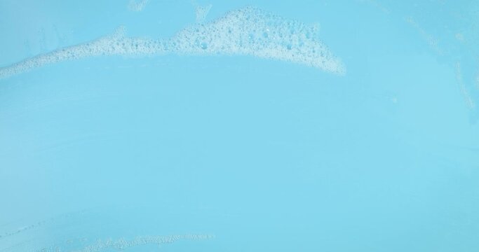 Hand in red rubber glove wipes soap cleansing foam out from the blue surface, cleaning concept