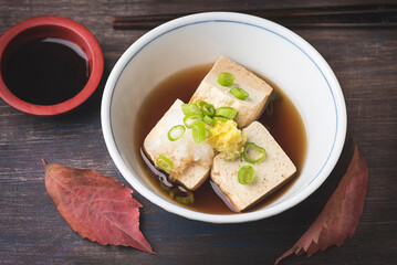 Autumn and winter hot Japanese recipe. Fresh hot tofu served with daikon, green onion,  chive ginger and soy sauce topping  on ceramic tradition blow  with chopsticks over wooden table. Top view
