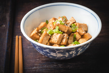 Autumn hot Japanese recipe. Fried tofu with sesame seeds, green onion and spices on ceramic plate with chopsticks,  wooden vintage background. Homemade healthy vegetarian Asia and Japanese dish