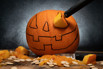 Halloween pumpkin carving with tools. Jack-o'-lantern spooky face drawing on whole orange autumn...
