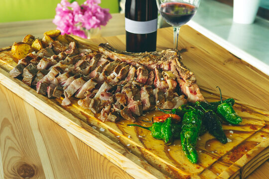 Juicy and appetizing sliced beef meat steak with potatoes and Padron peppers. Spanish Chuleton de Ternera. Grilled meat at wooden cutting board.