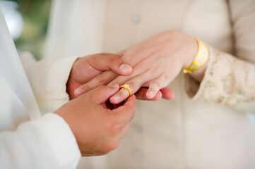 close up hand muslim groom in white dress waering wedding ring to left finger of muslim...