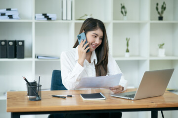 Asian businesswoman talking on the phone, working through a laptop, talking to customers online.