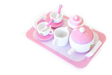 A set of pink white pastel color wood  toy tea cups including 2 coffee cups with teaspoons, a teapot, a sugar jar  and a milk jug is placed on a tray. Isolate clear on white background.