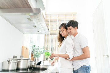 Fototapeta premium happy asian couple cooking healthy food. beautiful attractive girlfriend hugging by cheerful husband preparing healthy meal. couple cooking together for delightful beautiful healthy fresh good recipe
