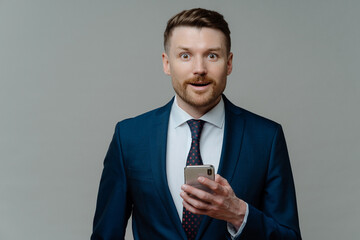 Amazed businessman in suit reading good news on smartphone