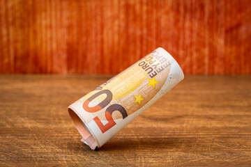 Roll of fifty euro banknotes falling on the wooden background
