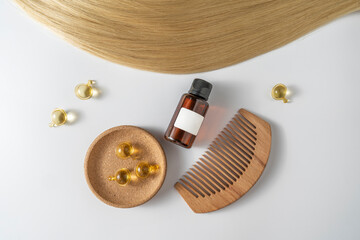 Fototapeta premium A hair care oil or serum in golden capsules lying on a strand of blond hair, product marketing mockup. A concept of hair care in a salon or at home