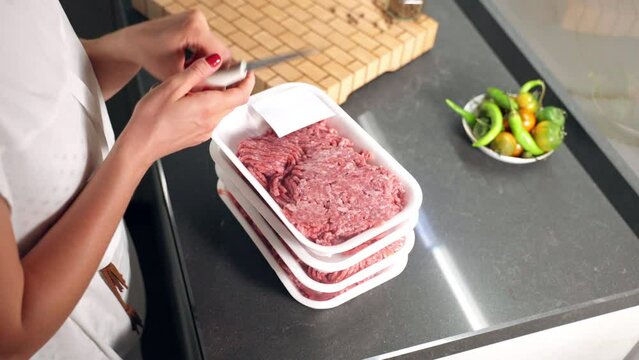 Woman bought raw minced meat at the supermarket, female unpacking plastic containers with mixed veal and beef meat cutting food film with cooking knife. Woman preparing mince for making home