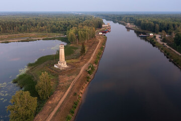 Fototapeta na wymiar Aerial view of long canal leading through forest with lighthouse and ferry crossing Dubna Russia