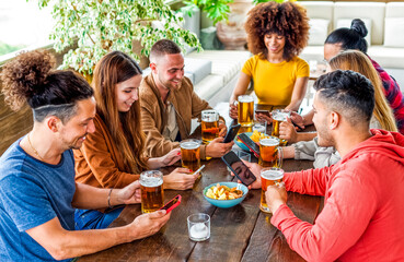 international group of friends drinking beer during happy hour vacation holidays. people having fun holding and looking the smartphone social media sitting in a pub restaurant table. lifestyle concept