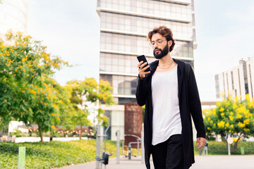 young man with beard walking by the city using a mobile phone, concept of urban lifestyle and...