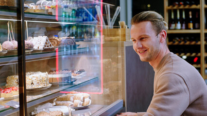 In the bakery cafe charismatic and good looking guy customer choose some dessert from the showcase fridge he is very excited
