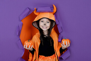 Little devil girl on a purple background is celebrating Halloween