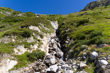 Fototapeta na wymiar Swiss mountain pass Sustenpass with meadow and mountain river on a sunny summer day. Photo taken July 13th, 2022, Susten Pass, Switzerland.