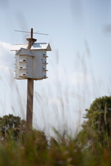 A handmade wooden bird hotel with many rooms for then to nest in.  This hotel sits upon a post in the middle of a large field.