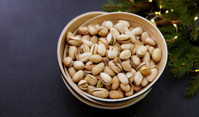 appetizing pistachio nuts in a peel in a wooden container close-up on a dark surface selective focus