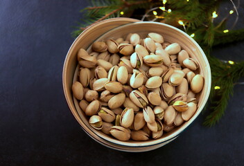 appetizing pistachio nuts in a peel in a wooden container close-up on a dark surface selective focus