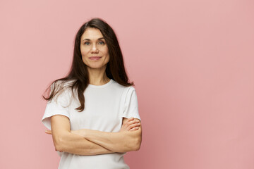 Obraz premium horizontal portrait of a cute, attractive woman on a pink background in a clean white t-shirt smiling pleasantly at the camera and folding her arms on her chest