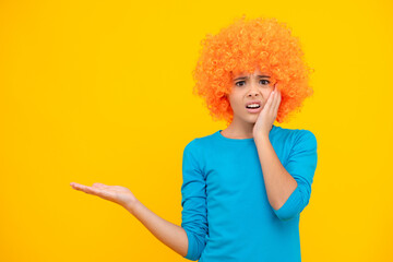 Funny kid in curly redhead wig. Time to have fun. Teen girl with orange hair, being a clown. Angry face, upset emotions of teenager girl.