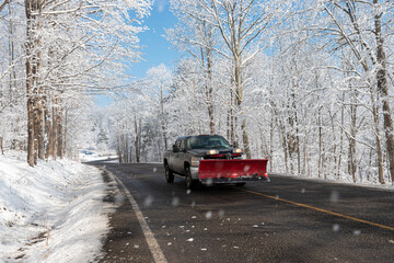 Snow is falling from the tree branches as this plow truck drives by.  White Winter Wonderland in...