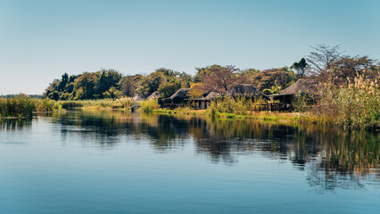 Idyllischer Blick auf eine Lodge am Ufer des Kwando River kurz nach Sonnenaufgang, Caprivi, Namibia