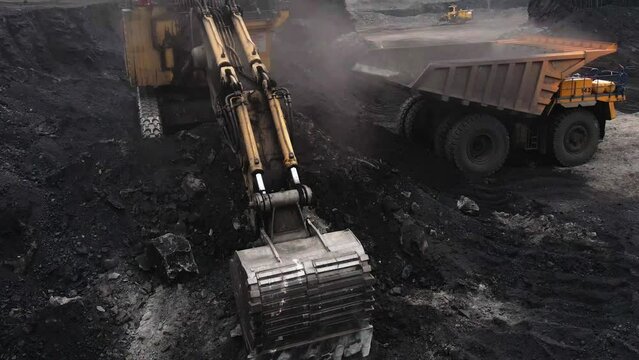 close-up of an excavator loading coal onto a yellow mining dump truck in a coal pit