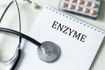 ENZYME text on a notebook on a table next to a stethoscope and tablets. Medical concept