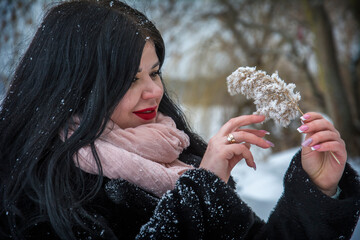 In winter, on a frosty cold day, a girl stands in the forest and holds a snow-covered spikelet in her hand.
