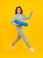 Run and jump. Full length of a fitness teen girl in sportswear hold yoga mat posing over yellow background. Fitness model child wearing sport clothes. Girl in the sport concept.