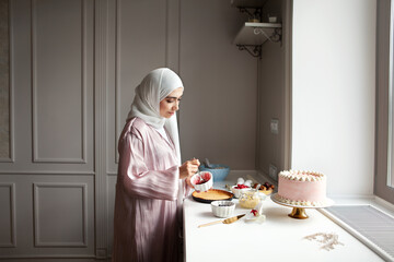 Muslim woman cooks dessert cake at home kitchen, arabian young model in hijab and abaya
