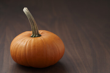 Small orange pumpkin on walnut wood table with copy space