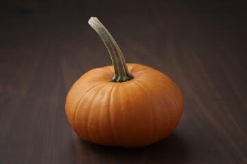 Small orange pumpkin on walnut wood table with copy space