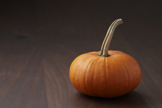 Small orange pumpkin on walnut wood table with copy space