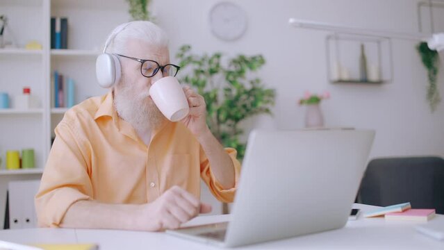 Happy senior man watching funny video on laptop, procrastinating at home