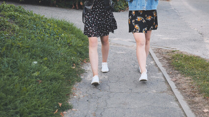 Two girlfriends in white sneakers walk down the street.