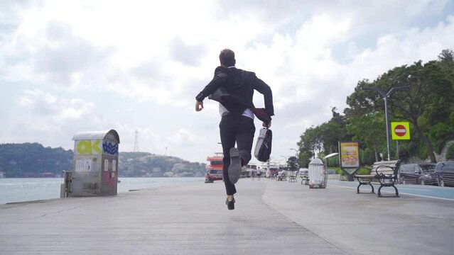 Man in suit is running by the sea. Slow motion.
Man in suit is running in the city by the sea. He is happy and opens his hands. He has her bag.

