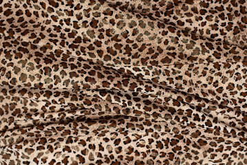 Bright background of fabric with a print of the skin of a wild animal - leopard or cheetah, dark brown spots on a light brown background, copy space