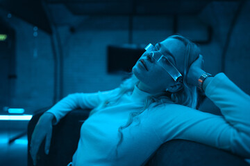 Neon blue light falls on a young woman wearing futuristic glass glasses.