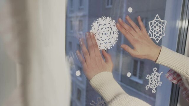 Teen girl sticks paper handmade snowflake on window glass in Christmas holiday eve