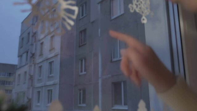 Girl blowing air to window glass and drawing small heart picture at home at winter evening