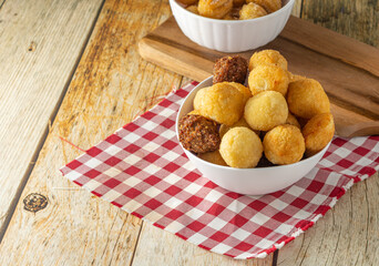brazilian salgadinhos de festa, traditional party snack mix with coxinha, kibe, and other fried snacks over wooden table in a white container