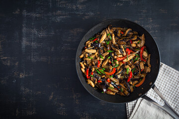 Stir fry with chicken, eggplant and pepper in wok pan on dark background