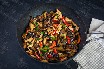 Stir fry with chicken, eggplant and pepper in wok pan on dark background