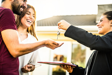 Happy millennial couple receiving keys from realtor, purchasing real estate - Family meeting with real estate agent - New house and real estate concept - obrazy, fototapety, plakaty