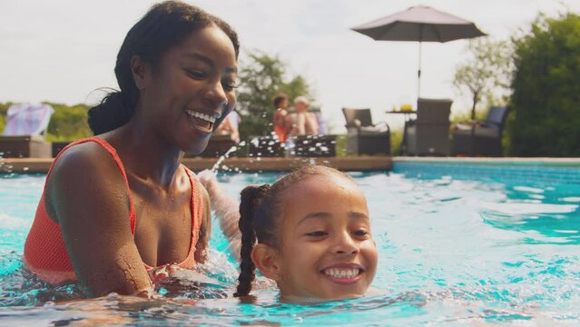 Parents and daughter splashing in outdoor swimming pool on family summer holiday - shot in slow motion