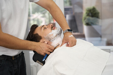 Obraz na płótnie Canvas Professional barber providing a shaving service for barbershop guest